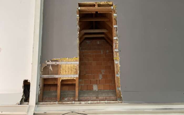 Offene Wandöffnung mit unverputztem Mauerwerk und ungedämmtem Dachanschluss in einer Gewerbeeinheit, sichtbar nach Rückbau der Innenverkleidung