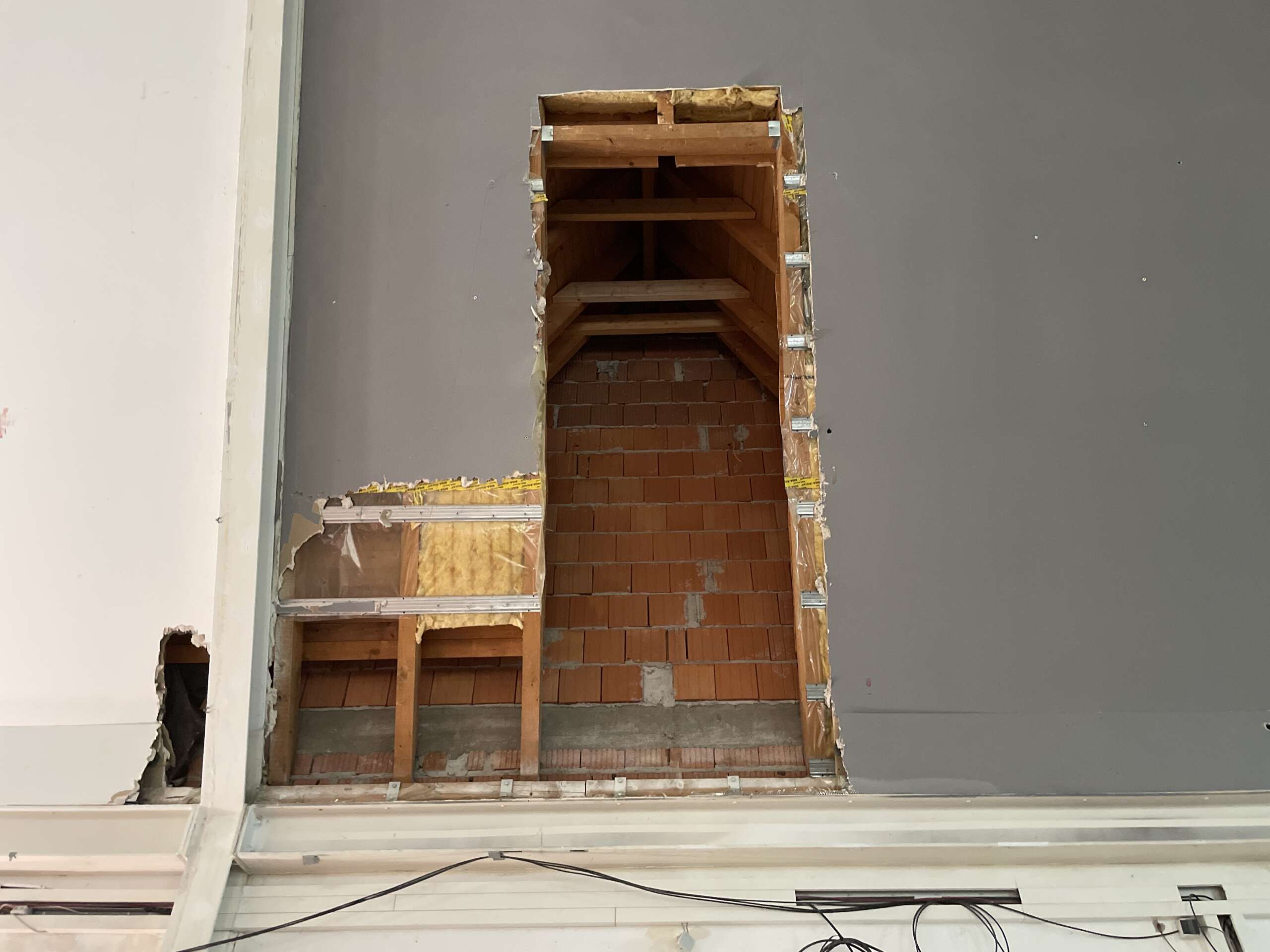 Offene Wandöffnung mit unverputztem Mauerwerk und ungedämmtem Dachanschluss in einer Gewerbeeinheit, sichtbar nach Rückbau der Innenverkleidung