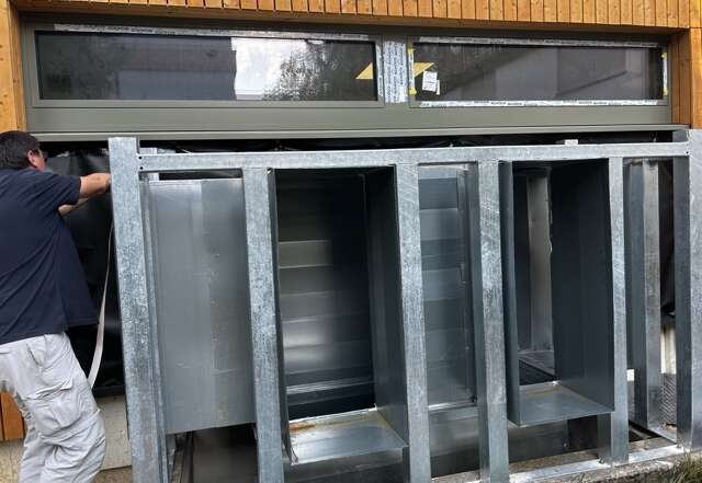 Mitarbeiter dichtet vor einem Blower-Door-Test Öffnungen einer großen Lüftungsanlage in einer Sporthalle provisorisch ab.