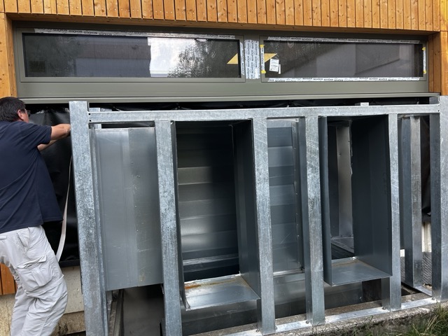 Mitarbeiter dichtet vor einem Blower-Door-Test Öffnungen einer großen Lüftungsanlage in einer Sporthalle provisorisch ab.